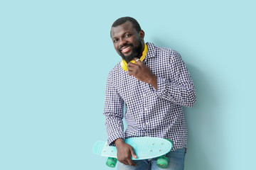 Handsome African-American man with headphones and skateboard on color background