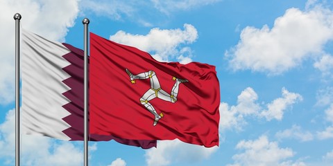 Qatar and Isle Of Man flag waving in the wind against white cloudy blue sky together. Diplomacy concept, international relations.