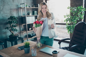 Photo of beautiful blond business lady came workplace morning holding little postcard read corporate party invitation fresh tulips bunch table modern cozy office