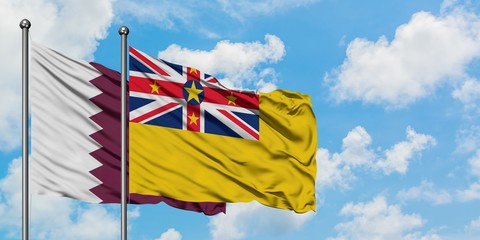 Qatar and Niue flag waving in the wind against white cloudy blue sky together. Diplomacy concept, international relations.