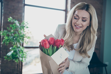 Photo of beautiful blond business lady came workplace looking fresh tulips bunch little postcard on table interested who is addresser read card modern office