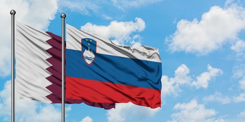 Qatar and Slovenia flag waving in the wind against white cloudy blue sky together. Diplomacy...