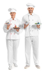Young confectioners with tasty desserts on white background