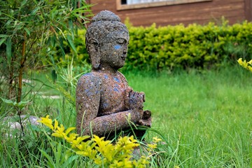 Obraz premium Cement made Buddha Statue among green grass and bamboo trees in garden 