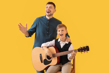 Handsome man and his little son with guitar on color background