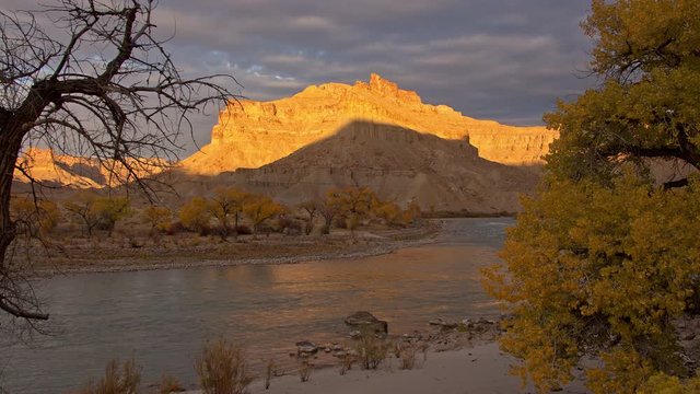 Sun shining on cliffs in the desert next to Green River in Utah looking past trees on Swaseys Beach.