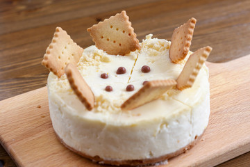A whole of classic New York cheesecake decorated with square cookies on plate, on wooden table in coffee pastry shop. Cake sweet dessert for holiday, birthday party. Cheesecake for the celebration clo