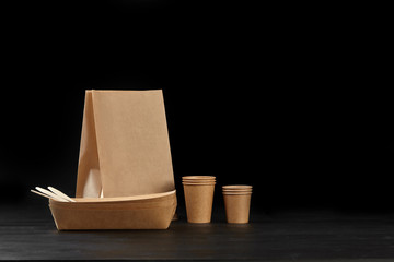 Eco friendly disposable tableware standing on dark surface against black background. Biodegradable craft dishes. Recycling concept. Close-up shot.