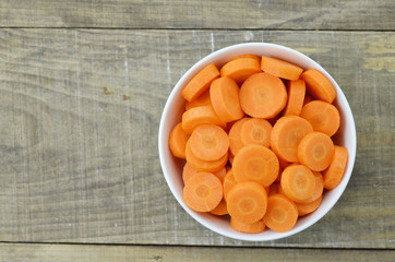 White bowl with cut carrots on wooden background