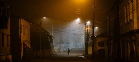 Lonely woman walking in foggy old city with street lights in a coat