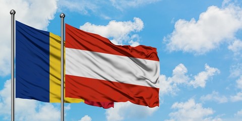 Romania and Austria flag waving in the wind against white cloudy blue sky together. Diplomacy...