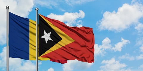 Romania and East Timor flag waving in the wind against white cloudy blue sky together. Diplomacy...
