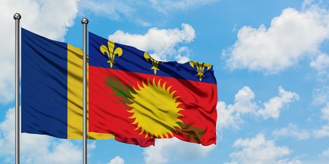 Romania and Guadeloupe flag waving in the wind against white cloudy blue sky together. Diplomacy concept, international relations.
