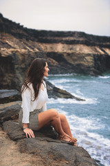 Mujer sentada en acantilado mirando al horizonte de mar océano
