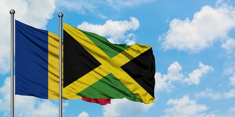 Romania and Jamaica flag waving in the wind against white cloudy blue sky together. Diplomacy...