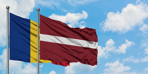 Romania and Latvia flag waving in the wind against white cloudy blue sky together. Diplomacy...