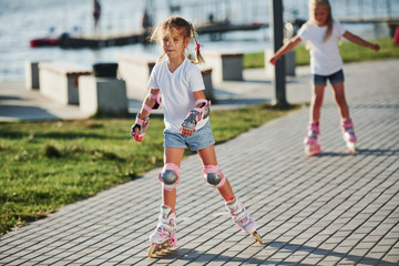 Two cute kids riding by roller skates in the park at daytime