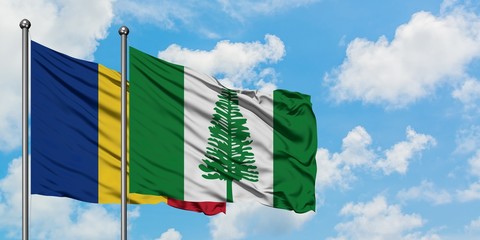 Romania and Norfolk Island flag waving in the wind against white cloudy blue sky together....