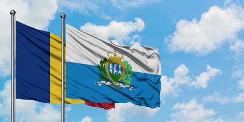Romania and San Marino flag waving in the wind against white cloudy blue sky together. Diplomacy...