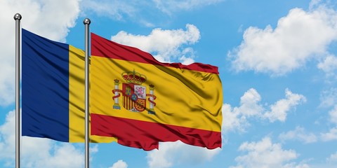 Romania and Spain flag waving in the wind against white cloudy blue sky together. Diplomacy...