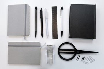 High angle top view of white desk with various black, gray and white neatly arranged working tools like scissors, pens, pencils and notebooks 