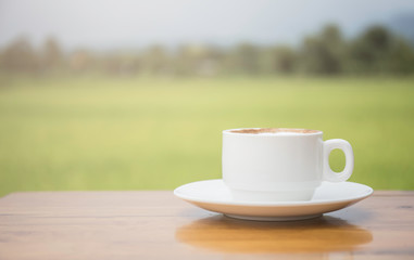 A white coffee cup on a wooden table With a backdrop of rice fields.