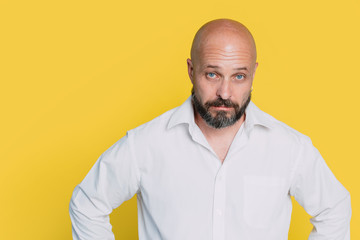 Fototapeta premium Serious middle-aged man with folded arms and a deadpan expression posing in front of a yellow background with copy space