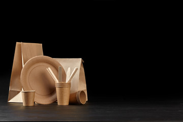 Eco friendly disposable tableware standing on dark surface against black background. Biodegradable craft dishes. Recycling concept. Close-up shot.