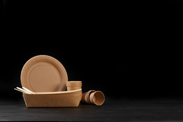 Eco friendly disposable tableware standing on dark surface against black background. Biodegradable craft dishes. Recycling concept. Close-up shot.