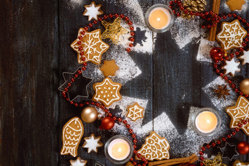 Gingerbread cookies, spices and burning candles on a star shape from icing sugar on a dark rustic wooden background, Christmas composition with copy space, high angle view from above