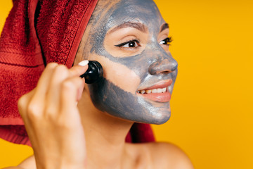 girl beautician client with a black charcoal mask on her face, smiles and leads a chess piece on her cheek. studio yellow