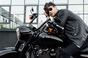 Fototapeta na wymiar handsome young man in leather jacket resting while sitting on new black motorcycle