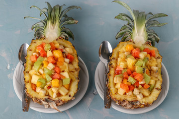 Tropical fruit salad in pineapple halves on white plates on a light blue background, Top view