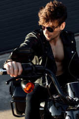 Fototapeta na wymiar young man sitting on motorcycle in sunlight, holding handle and looking away