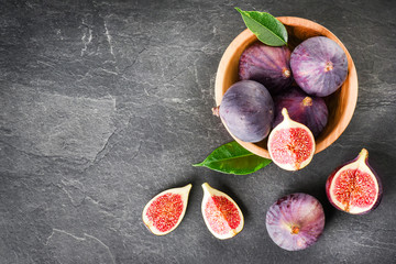 Fresh figs in round wooden bowl on stone table. Ripe fig fruits with leaves on black texture board...
