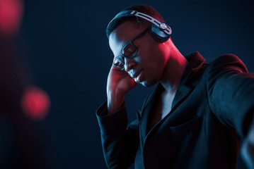 Enjoying listening music in headphones. In glasses. Futuristic neon lighting. Young african american man in the studio