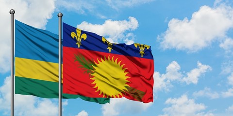Rwanda and Guadeloupe flag waving in the wind against white cloudy blue sky together. Diplomacy...