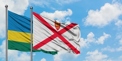 Rwanda and Jersey flag waving in the wind against white cloudy blue sky together. Diplomacy...
