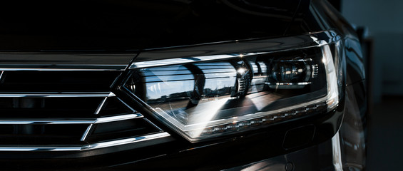 Front part of brand new modern car. Parked at showroom. Reflection in the headlights
