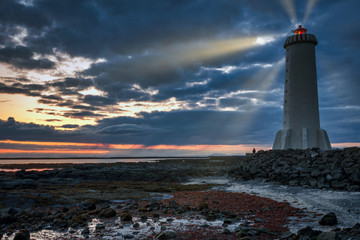 Man sitting next to Akranesviti lighthouse at night, watching the beautiful sunset view. Light...