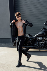 Fototapeta na wymiar handsome young man taking off leather jacket while walking near motorcycle