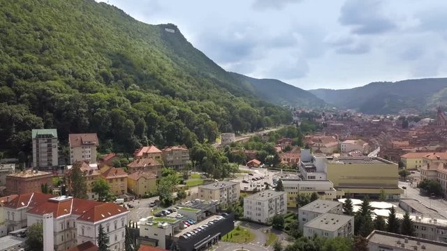 Aerial view of Brasov city, medieval town situated in Transylvania, Romania. Old architecture surrounded with big Carpathian mountains covered with dense green forest.