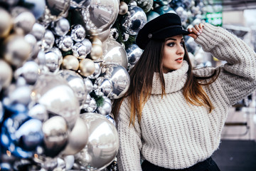  young woman in warm oversize sweater posing near christmas decorations outdoor
