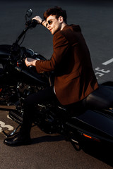 Fototapeta na wymiar motorcyclist in brown jacket and sunglasses sitting on motorcycle and holding handlebars