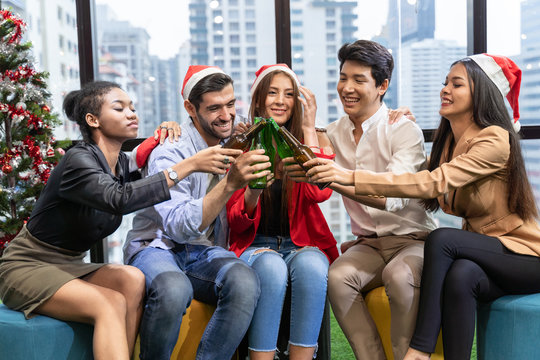 Office Christmas Party. Merry Christmas And Happy New Year Multiracial Young Creative People Are Celebrating Holiday In Modern Office. Group Of Young Business People Are Drinking Champagne