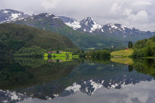 Beautiful Norwegian landscape scenery from Storevatnet in Fyrde/Volda/M&Atilde;&cedil;re og romsdalen in Norway. The snow covered mountains and a little farm reflects in the calm water.