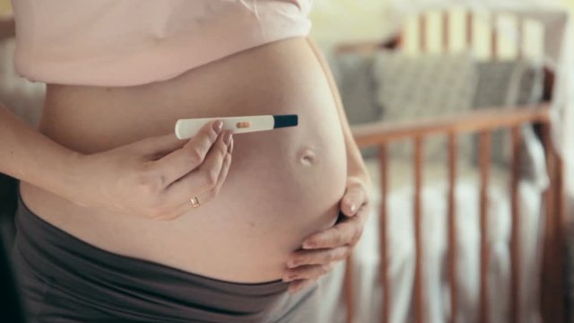 Close-up shot of big pregnant tummy and woman's hands holding pregnancy test. Women's health and people concept. Maternity prenatal care and woman pregnancy concept.