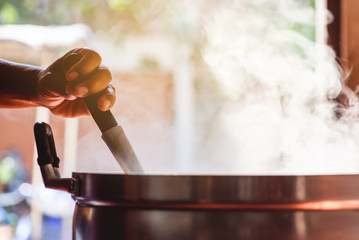 Cooking person in the restaurant is cooking while using the dipper in a large pot. And the water is boiling, there is smoke, hot spit.
