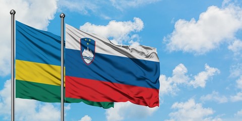 Rwanda and Slovenia flag waving in the wind against white cloudy blue sky together. Diplomacy...