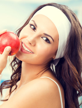 Cheerful young lovely woman with red apple, at fitness center or gym